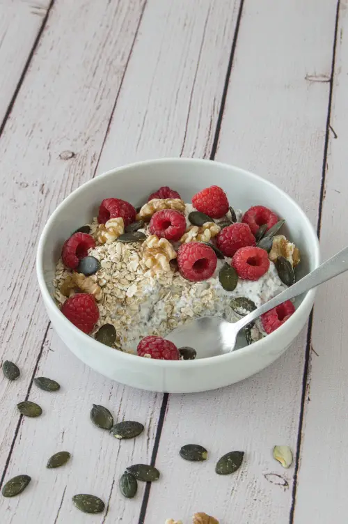 Petit-déjeuner au skyr, avoine et framboises IG bas Cuillère dans un bol de skyr avec avoine, framboises, noix et graines de courge.
