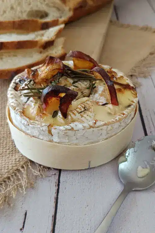 Camembert rôti IG bas : la recette d'automne aux pommes Gros plan sur un camembert rôti aux tranches de pomme dorées, au romarin et au thym, fromage fondu au centre. Camembert rôti IG bas