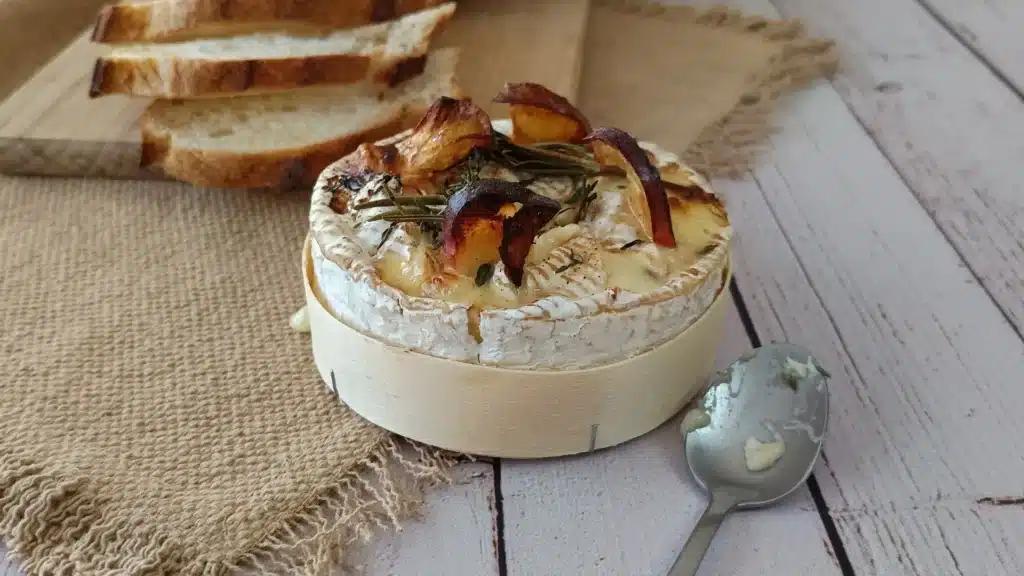Camembert rôti IG bas : la recette d'automne aux pommes Camembert rôti IG bas dans sa boîte en bois, avec tranches de pomme, romarin et thym, et pain tranché en arrière-plan