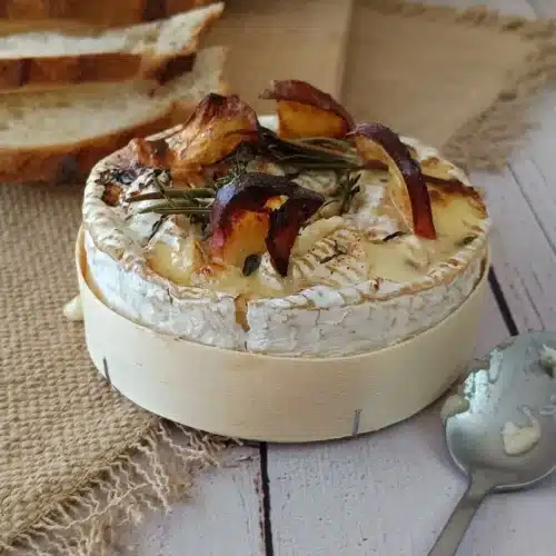 Camembert rôti IG bas : la recette d'automne aux pommes Camembert rôti IG bas dans sa boîte en bois, avec tranches de pomme, romarin et thym, et pain tranché en arrière-plan